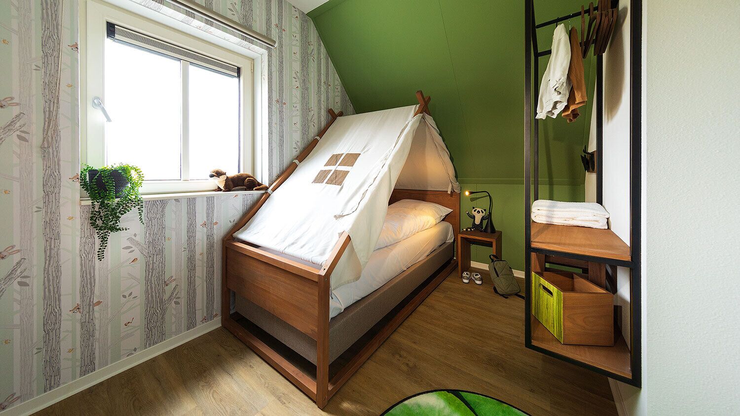 A bedroom with a wooden bed, a window with a view, a green wall, and a shelf with clothes.