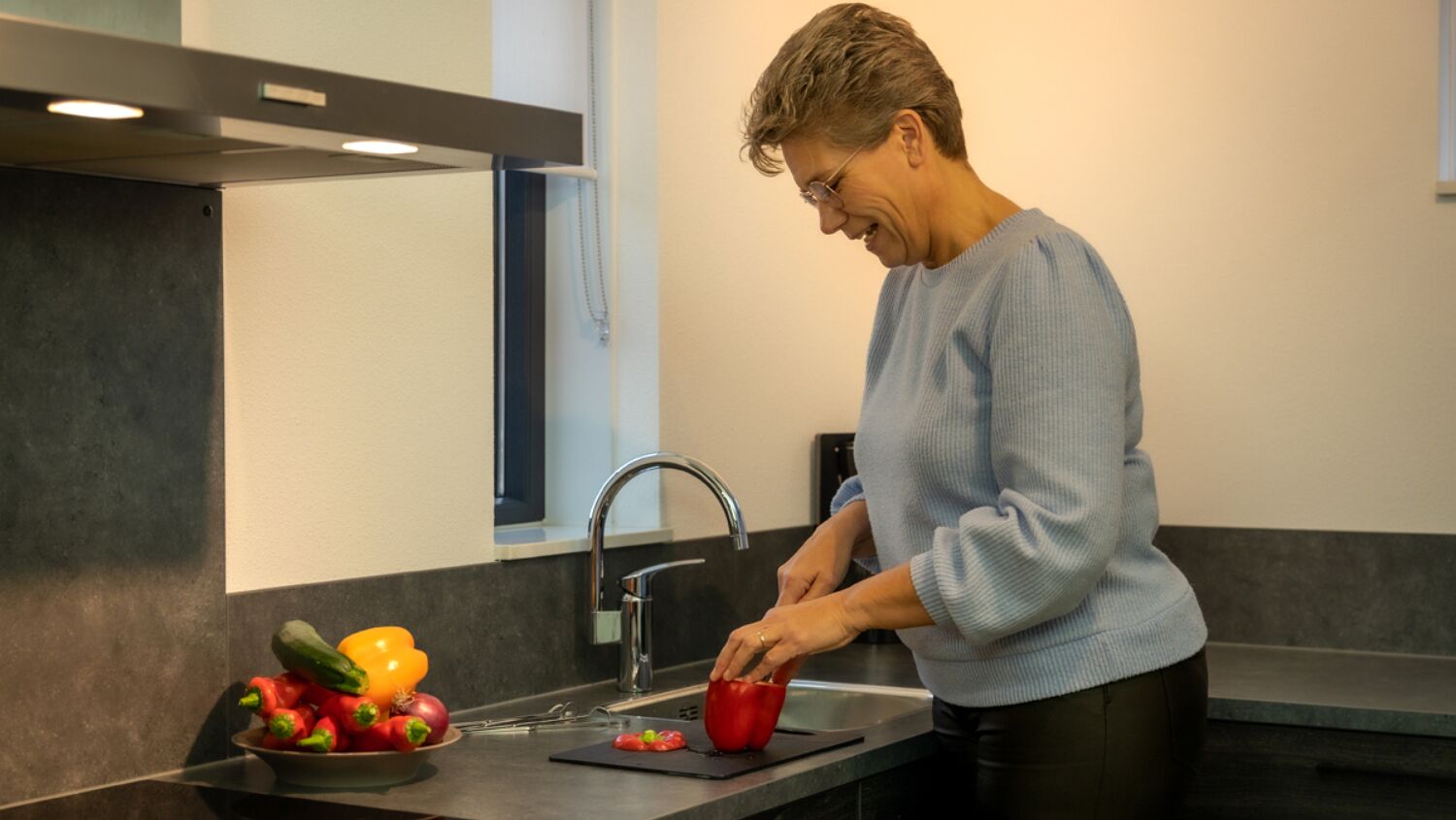Een persoon bereidt eten in een moderne keuken met een spoelbak, aanrecht en een schaal groenten.
