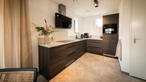 A modern kitchen with dark wood cabinetry, a built-in microwave, and a large island with a sink. - Luxe 6p - Three Bedroom Villa, Sleeps 6 (Thorn)