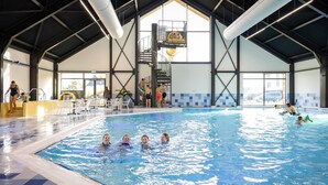An indoor swimming pool with a high ceiling, a central staircase, and a seating area with tables and chairs. - Luxe 6p - Three Bedroom Villa, Sleeps 6 (Thorn)