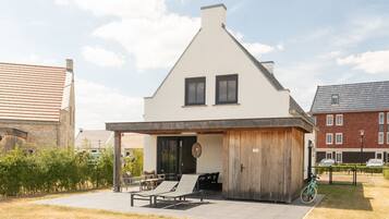 A modern two-story house with a covered patio, a wooden door, and a bicycle parked outside.