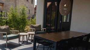 Eine Terrasse im Freien mit einem Holztisch und Stühlen, einer hängenden Leuchte und einer Ziegelwand im Hintergrund.