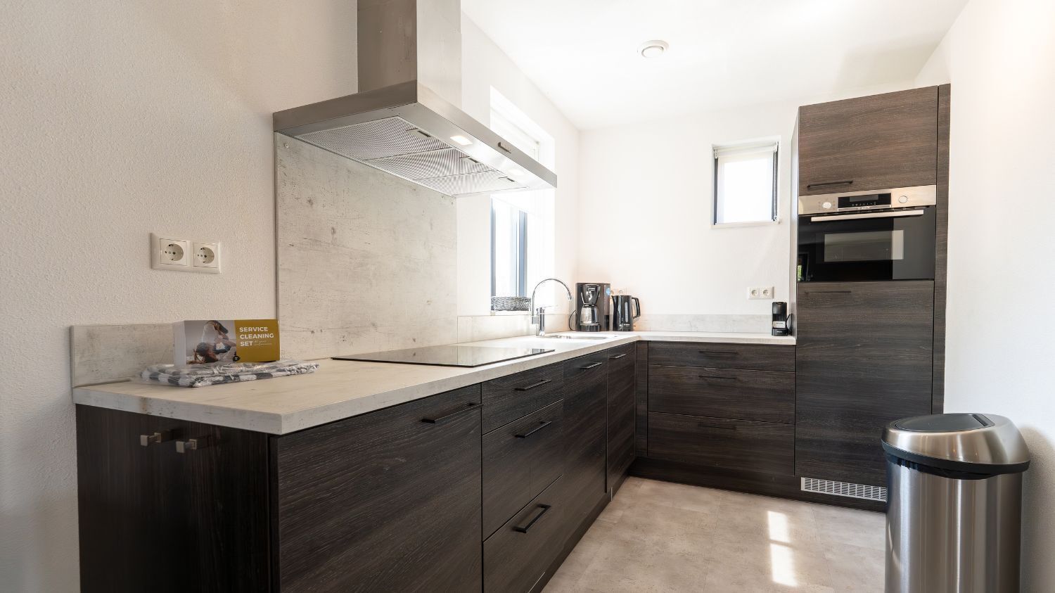 A modern kitchen with dark wood cabinets, a stainless steel range hood, and a built-in oven.
