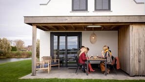 Un espace extérieur aménagé pour les repas, avec une table et des chaises, une pergola en bois et une vue sur un lac.