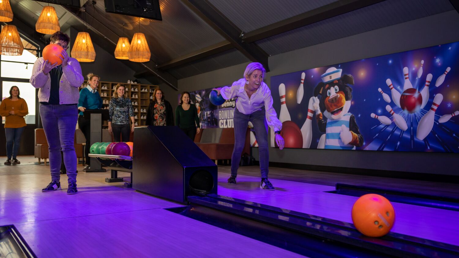 A bowling alley with a person bowling, a bowling ball in motion, and a bowling pin set up.