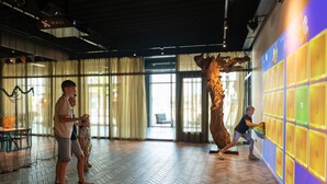 Um quarto espaçoso com piso em padrão herringbone, uma grande escultura de madeira e uma parede com painéis iluminados.