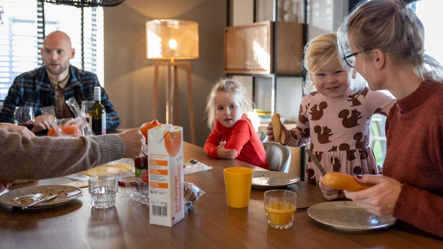 A family dining at a wooden table with various food items and drinks.