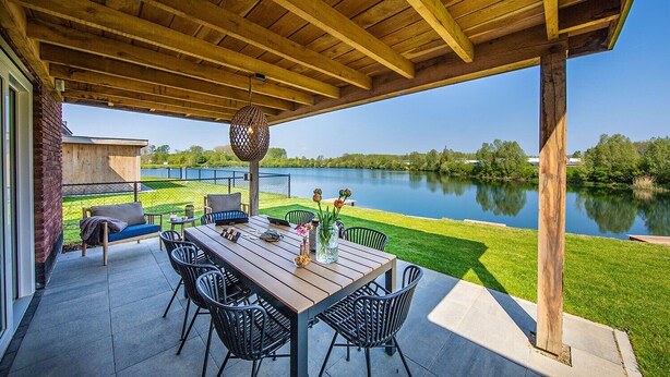 Un patio al aire libre con una mesa y sillas de madera, un colgante de luz y vista a un lago.
