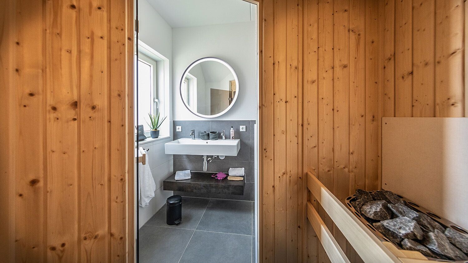 A wooden-paneled bathroom with a sink, mirror, and a small trash bin.