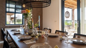 Une table à manger dressée avec des assiettes, des couverts et des bougies, agrémentée d’un vase de fleurs et d’un luminaire suspendu.