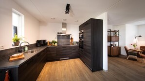 Une cuisine moderne avec des meubles de couleur sombre, un plancher en bois et un four encastré.