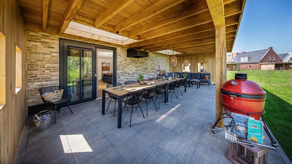 Un patio al aire libre con mesa y sillas de madera, una parrilla y un muro de piedra.