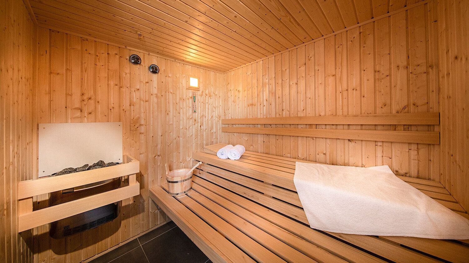 Una sauna de madera con bancos, un banco con una toalla y un pequeño estante de madera con piedras.