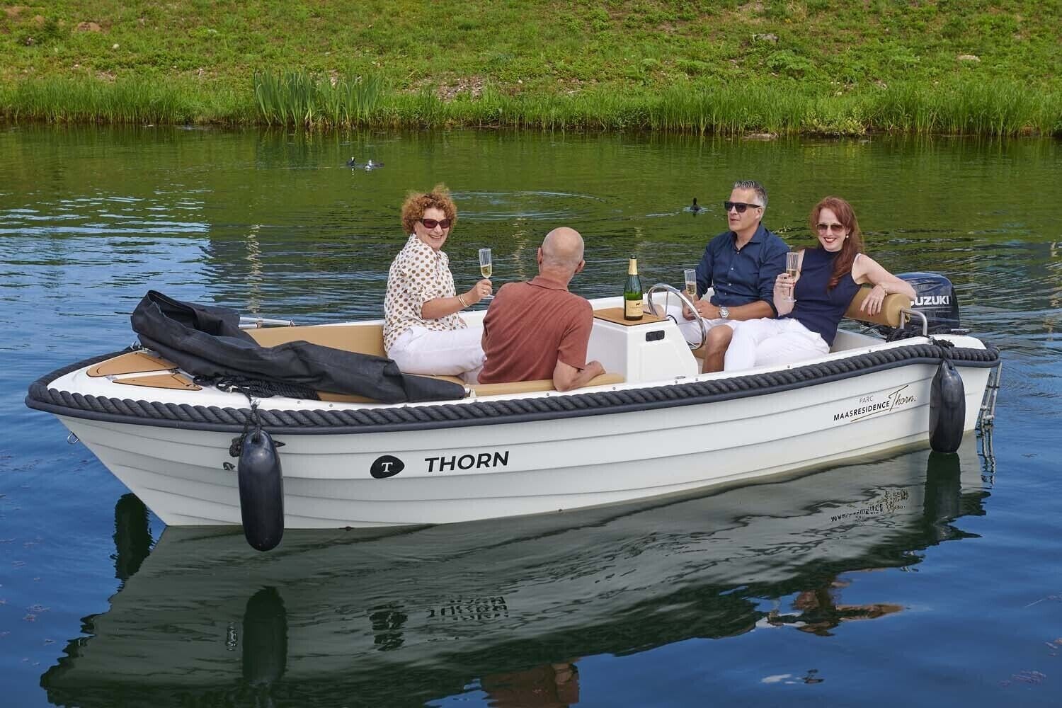 Ein kleines Motorboot namens 'THORN' mit vier Personen an Bord, einer Champagnerflasche und einer Tasche.