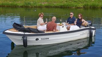 Ein kleines Motorboot namens 'THORN' mit vier Personen an Bord, einer Champagnerflasche und einer Tasche.