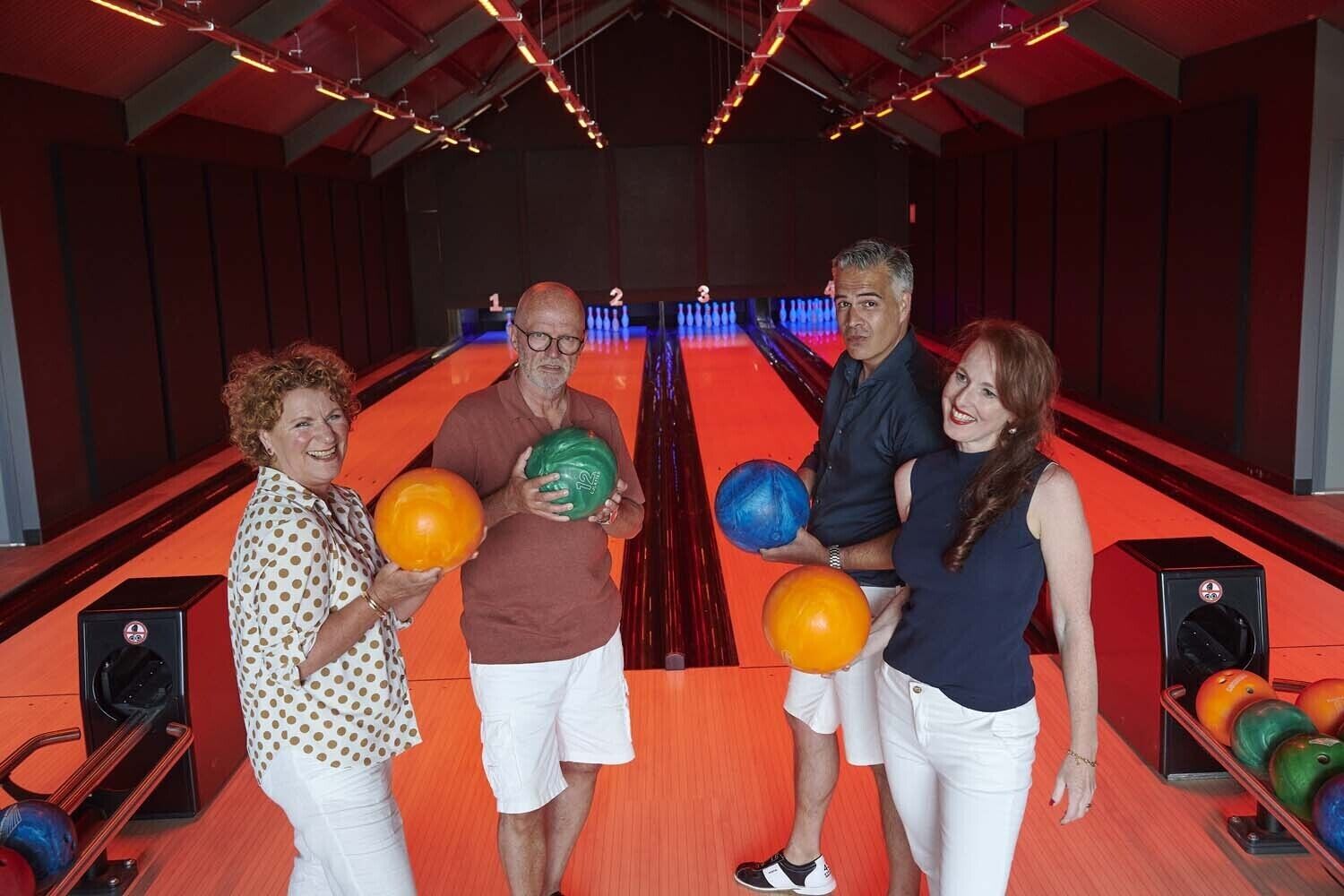 A bowling alley with four people holding bowling balls, a bowling lane, and a bowling ball rack.
