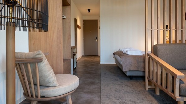 A modern hotel room with a wooden chair, a bed with a grey headboard, and a small table. - Lake View Hotel Room 2p (Thorn)