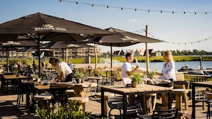 An outdoor dining area with wooden tables and chairs, black umbrellas, and a view of a lake. - Lake View Hotel Room 2p (Thorn)