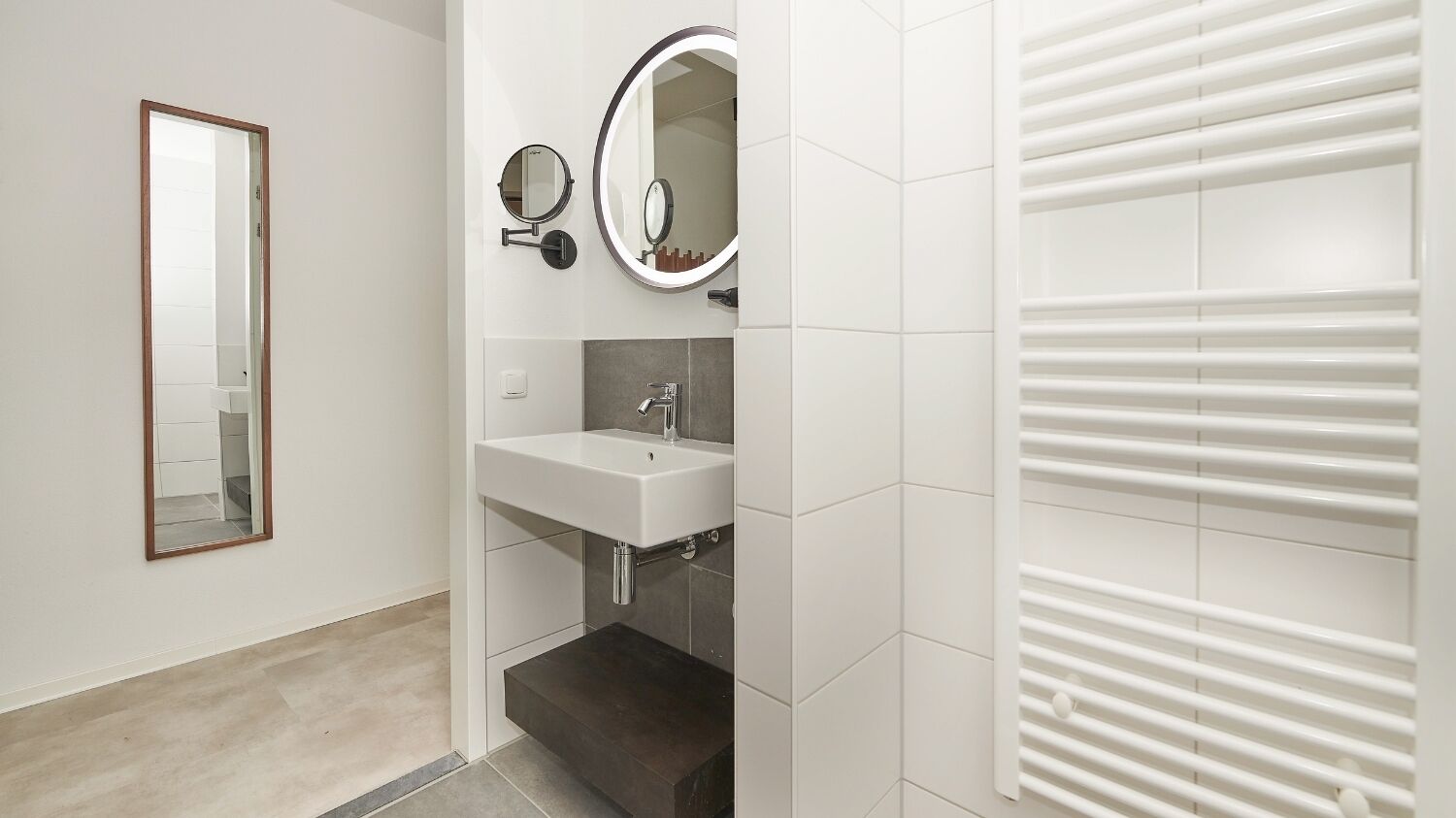 Une salle de bain moderne avec un lavabo blanc, deux miroirs fixés au mur et un porte-serviettes.