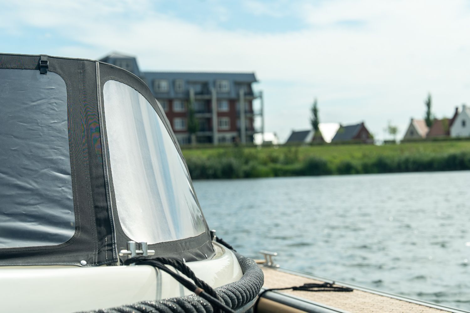 Ein Boot mit überdachtem Deck, einer Leine und Blick auf einen Fluss mit Gebäuden im Hintergrund.