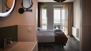 A hotel room with a bed, a bathroom with a sink, and a view of a balcony. - Lake View Maisonette 4p (Thorn)