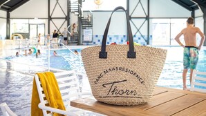 A poolside area with a woven bag labeled "MAASRESIDENCE Thoreau" on a wooden table. - Lake View Maisonette 4p (Thorn)