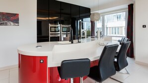 A modern kitchen with a central island, black bar stools, and a large window with curtains. - Hyde Park Heights, by Veeve (London)
