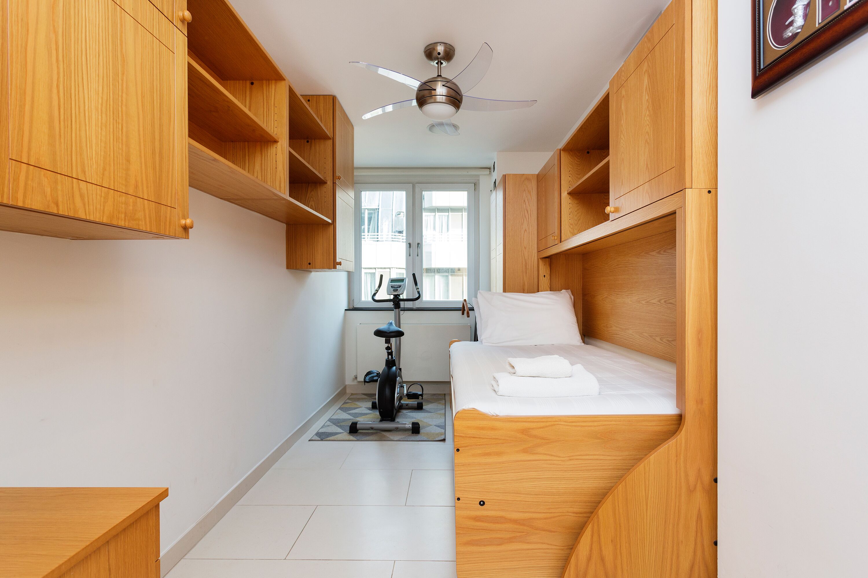 Ein gemütlicher Raum mit Bett, Holzschränken, Deckenventilator und einem Heimtrainer.
