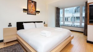 A modern hotel room with a large bed, a painting above the bed, and a view of a building through the window. - Hyde Park Heights, by Veeve (London)