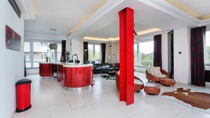 A modern living space with a kitchen island, a red accent column, leather furniture, and a cowhide rug. - Hyde Park Heights, by Veeve (London)