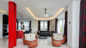 A modern living room with a sofa set, a red accent wall, and a kitchen in the background. - Hyde Park Heights, by Veeve (London)