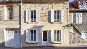 Ein zweistöckiges Gebäude mit Steinaußenwand, weißen Fensterläden und einem kleinen Balkon mit Blumen.