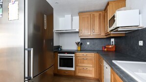 Eine kompakte Küche mit Edelstahlkühlschrank, integriertem Backofen, Holzschränken, einer Mikrowelle und einer schwarzen Arbeitsplatte.