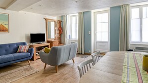 Ein modernes Wohnzimmer mit Sofa, Sessel, Fernseher und Esstisch.