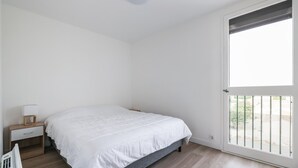 A bedroom with a bed, a nightstand, a window with a view, and a door. - Ombeline - Apt proche mer avec balcon (Saint-Cyprien)