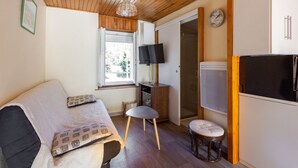 Et hyggeligt rum med sofa, en lille skammel, fjernsyn og køleskab.