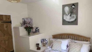 Un dormitorio con cabecera de madera, cama con ropa de cama floral, estante con objetos decorativos y un cuadro en la pared.