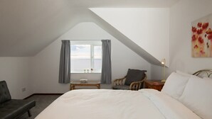 Een slaapkamer met een groot bed, een kleine tafel, een stoel en een raam met gordijnen.