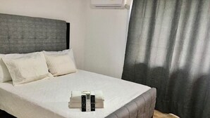 Una cama bien hecha con cabecera gris, ropa de cama blanca y un control remoto sobre la cama.