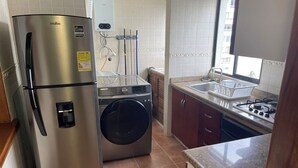 Una cocina compacta con un refrigerador de acero inoxidable, una lavadora, una estufa a gas y un lavamanos.