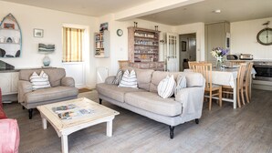 A spacious living room with a beige sofa set, a coffee table, and a dining area with wooden chairs and a table. - Atlantis (Wadebridge)