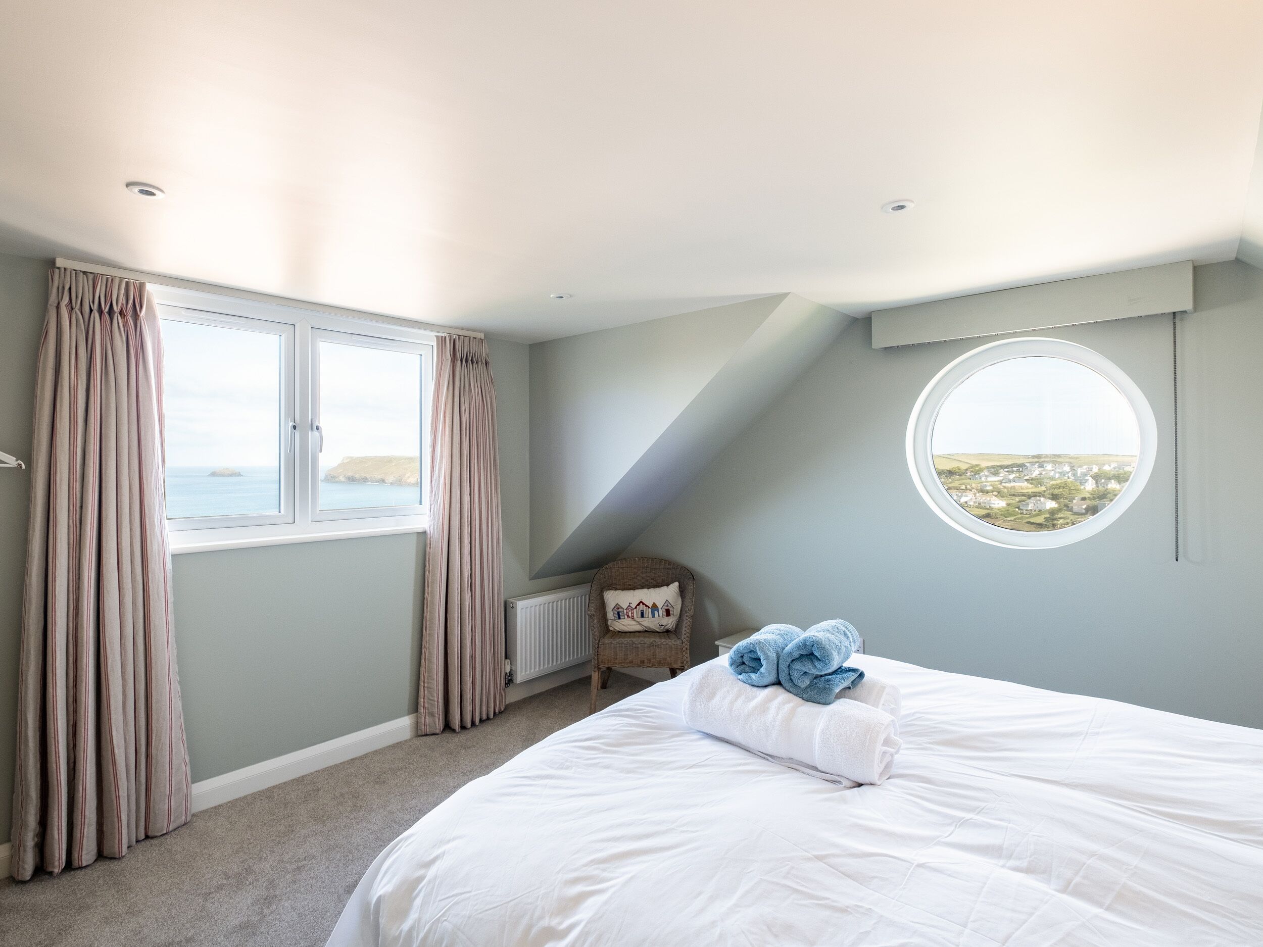 Une chambre avec une grande fenêtre, un puits de lumière circulaire et une vue sur la mer.