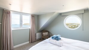 A bedroom with a large window, a round skylight, and a view of the sea. - Atlantis (Wadebridge)