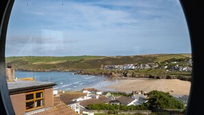 A coastal town with houses, a beach, and hills in the background. - Atlantis (Wadebridge)
