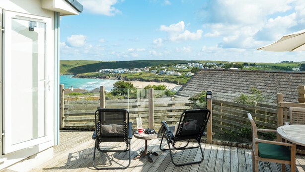 A deck with two chairs and a table, overlooking a coastal view with houses and hills. - Atlantis (Wadebridge)