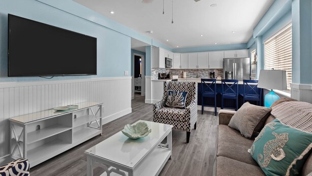 Un soggiorno moderno con una televisione a schermo piatto, una ventola a soffitto e un'area pranzo con sedie blu.