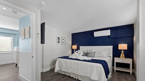 Camera da letto con un letto bianco, parete di un blu scuro e un comodino bianco con una lampada.
