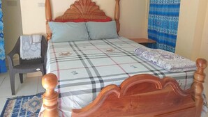 Un dormitorio con una cama de madera, una mesita de noche, una silla y un edredón estampado.