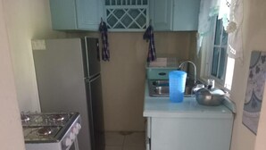 Cocina compacta con estufa a gas, refrigerador y pileta. Hay un recipiente de plástico azul sobre la encimera.
