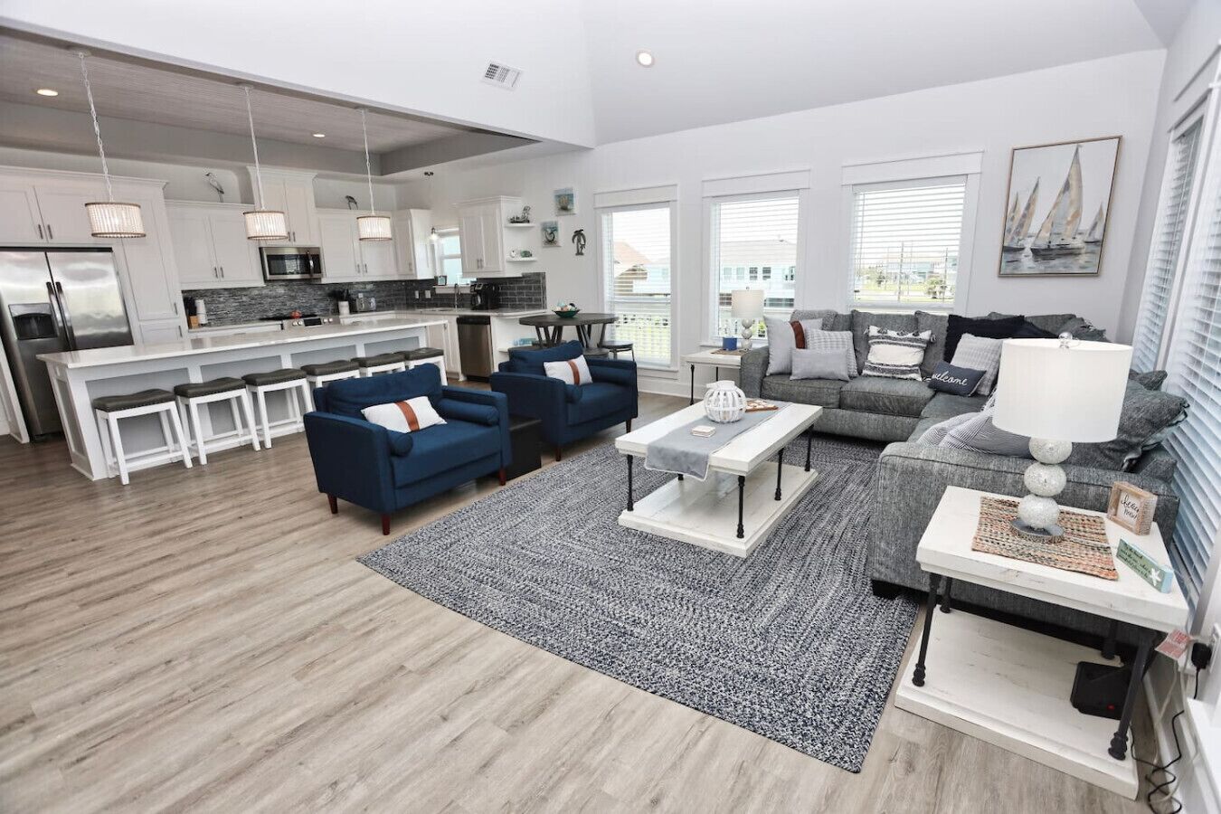 A spacious living area with a kitchen, grey sofas, a coffee table, and a view of the outside.